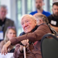 President Emeritus Don Lubbers listens to rowing speech while rest arm on cane